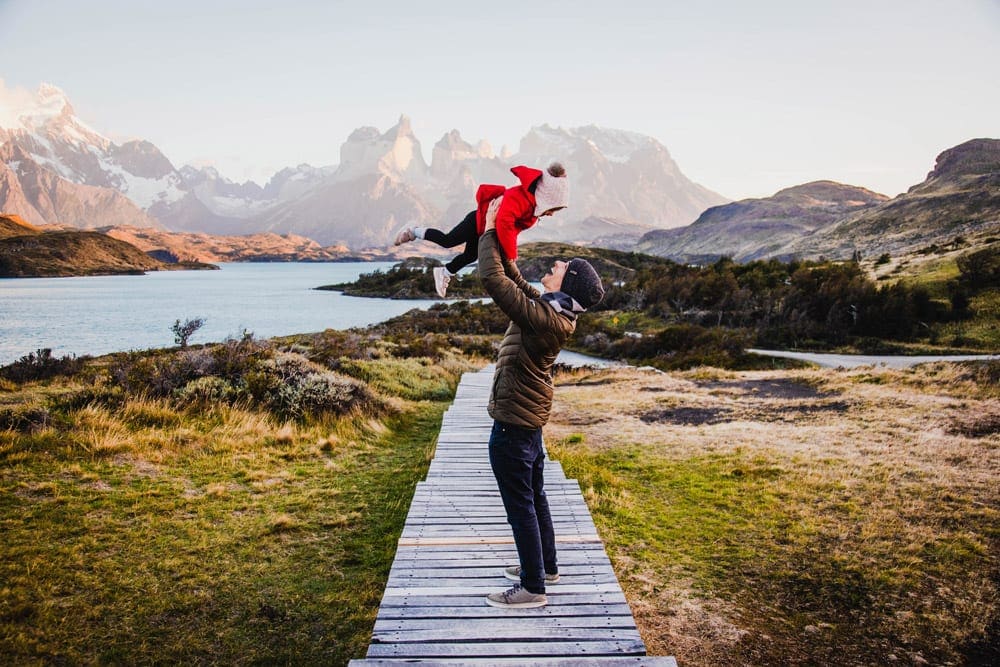 A dad holds his young daughter over his head while wander a boardwalk in Chile.