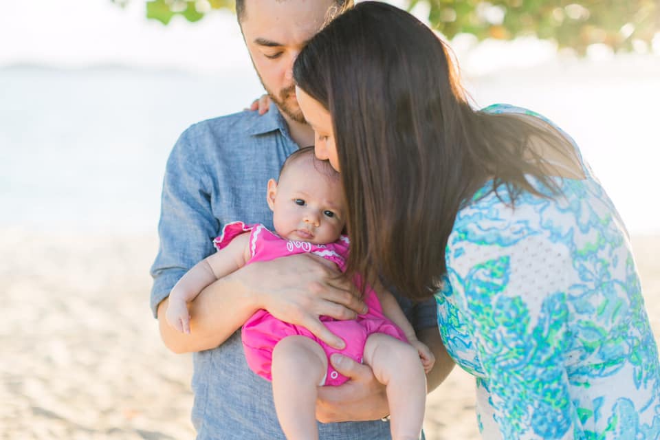 A mom and day hold and kiss their infant daughter while on the beach at St. Thomas, one of many warm spring break family destinations.