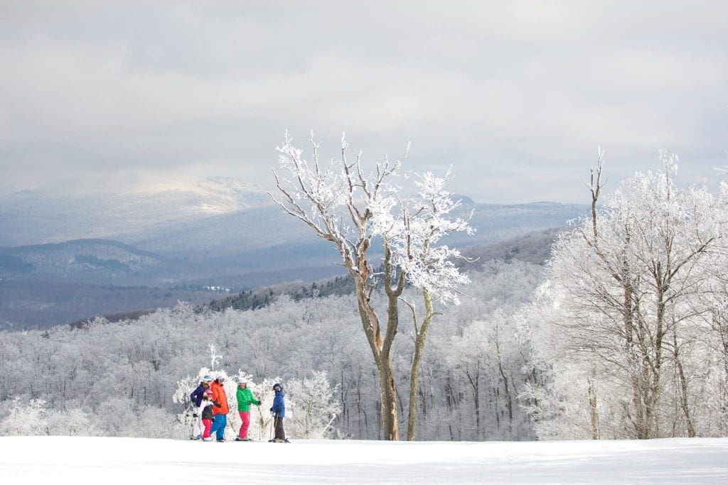 Several skiers, decked out in vibrant gear, stand mountainside in the snow while skiing at Jiminy Peak Mountain Resort, one of the best ski resorts in the United States for families.