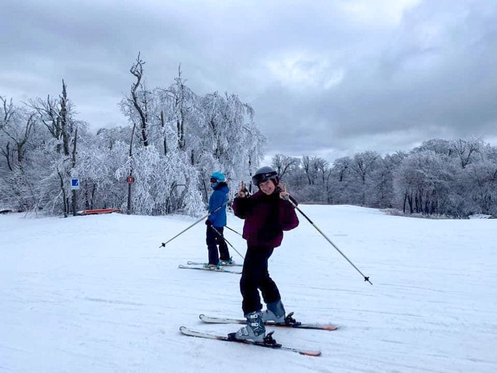 A teenager on skis holds up two peace signs while smiling at Belleayre Mountain, one of the best ski resorts near NYC for families.