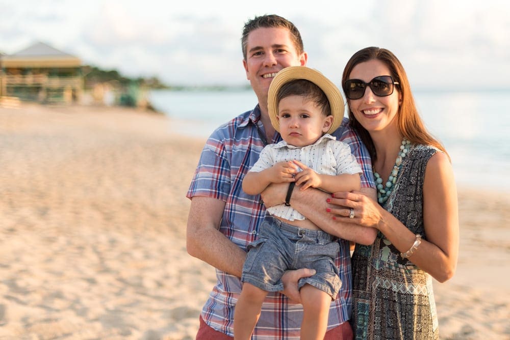 Two parents and one kid smile on the beach in Antigua.