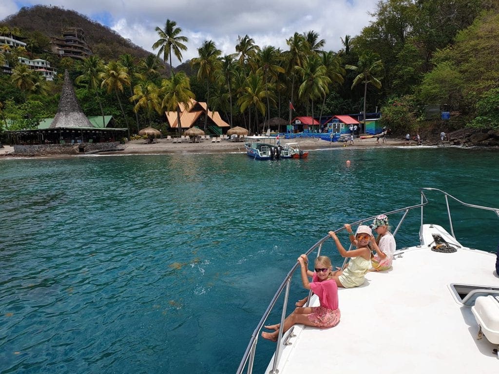 Three kids sit on the deck of a boat in a bay, off the shore of St. Lucia.