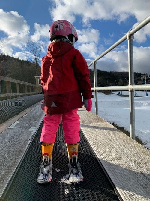 A young girl on skis takes a carpet lift at Blue Mountain.