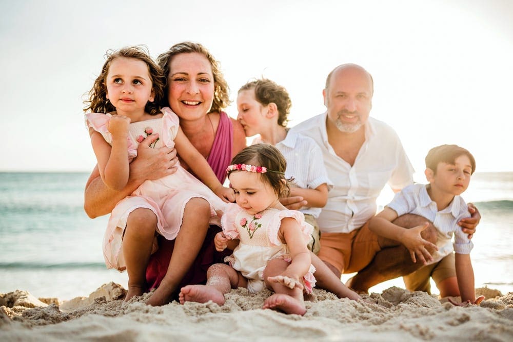 A family of six snuggles together smiling on the beach in Aruba, one of the best Caribbean Islands for Families.