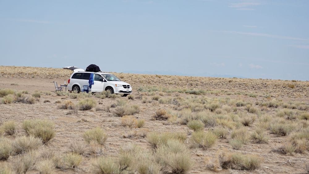 A car is parked with a wide view of sand dunes around it.