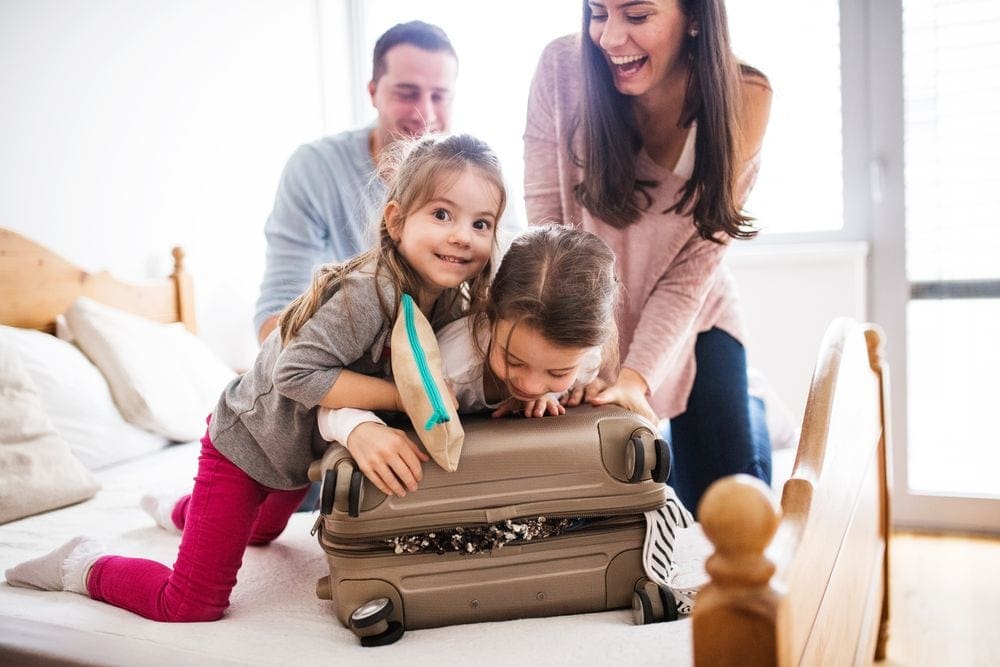 A family of four sits on a bed packing a suitcase.