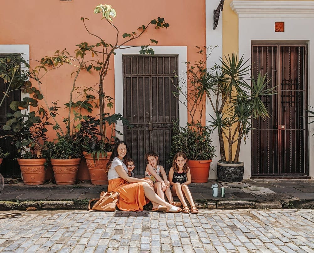 A mom sits with her three children on a stoop surrounded by tropical plants in Puerto Rico.