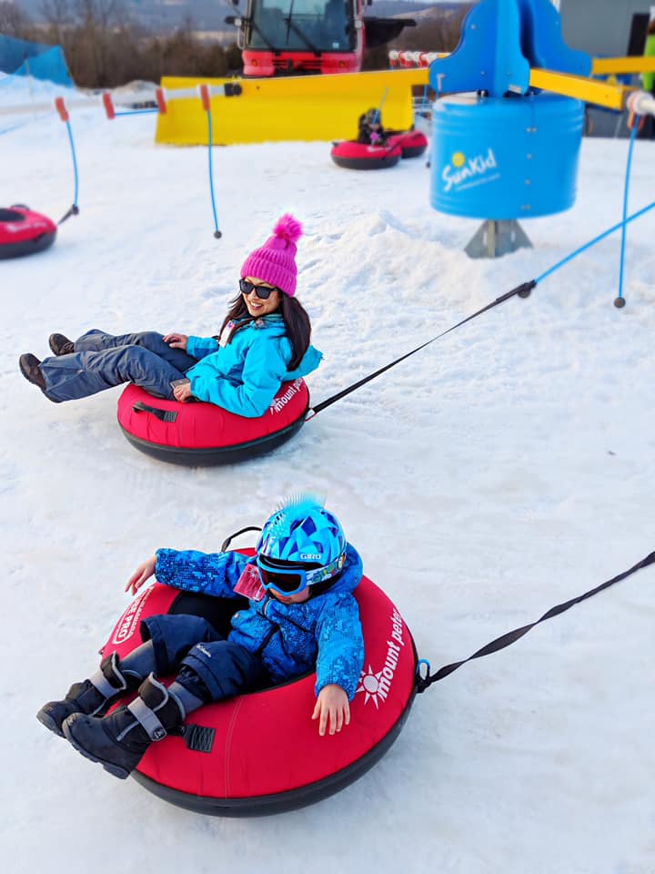 Mom and son sit in their own red snow tubes while enjoying a sunny day at Mount Peter.