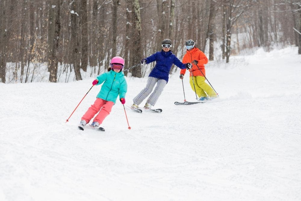 Three skiers, all wearing brightly colored snow gear, ski down a run at Windham Mountain Ski Resort, one of the best ski resorts near NYC for families.