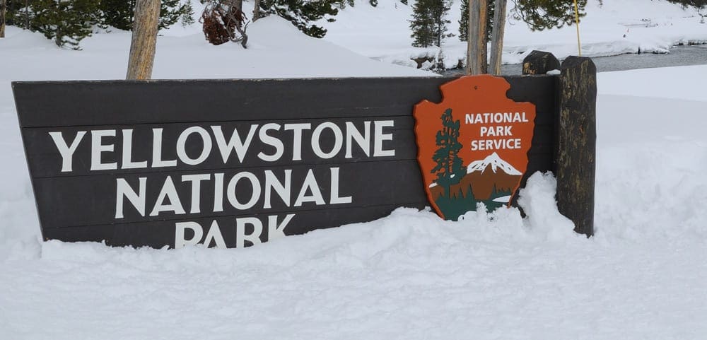 The sign for Yellowstone National Park covered in snow, which you can see during your  skiing trip to Big Sky with kids.