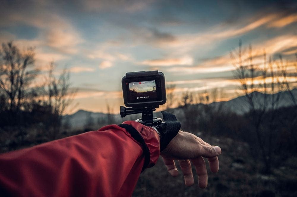 An arm wearing a red jacket reaches out wiht a GoPro on the wrist, filming a nature scene.