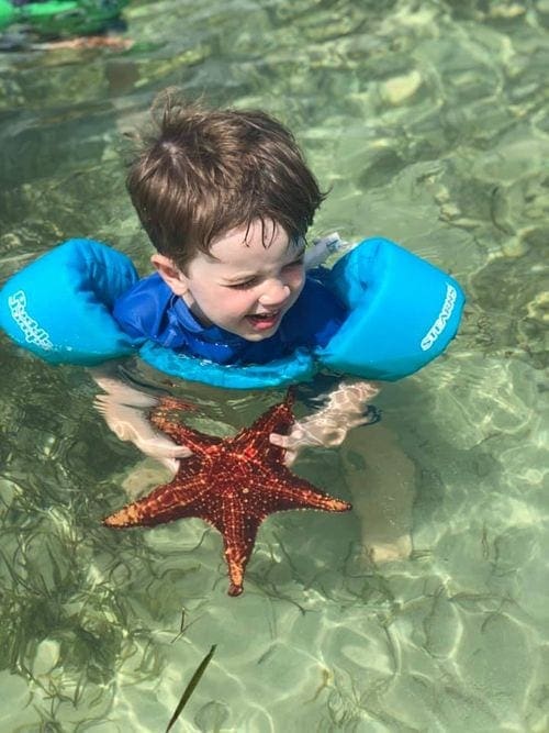 A young boy wearing blue floaties holds a starfish at Starfish Point.