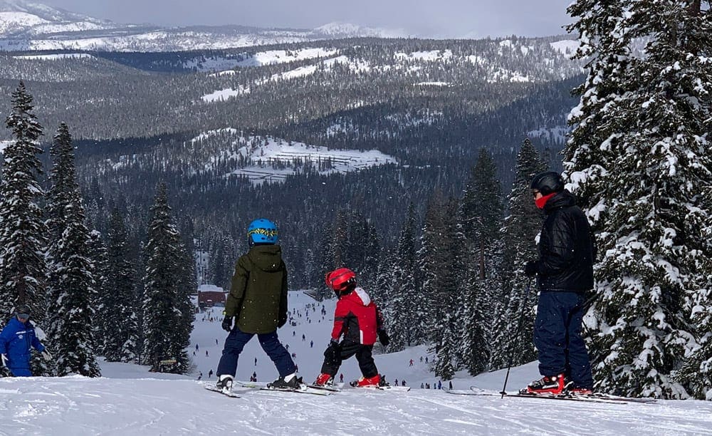 One adult and two child skiers look down the slope at Squadron.