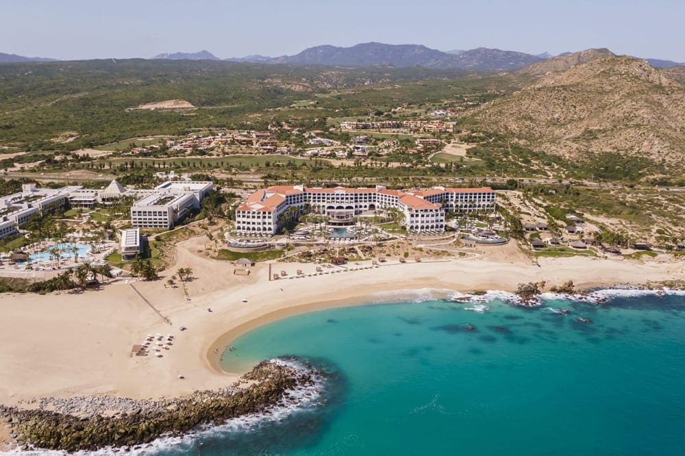 An aerial view of Hilton Los Cabos Beach and Golf Resort, featuring turquoise waters, sandy beach, and hotle buidlings.