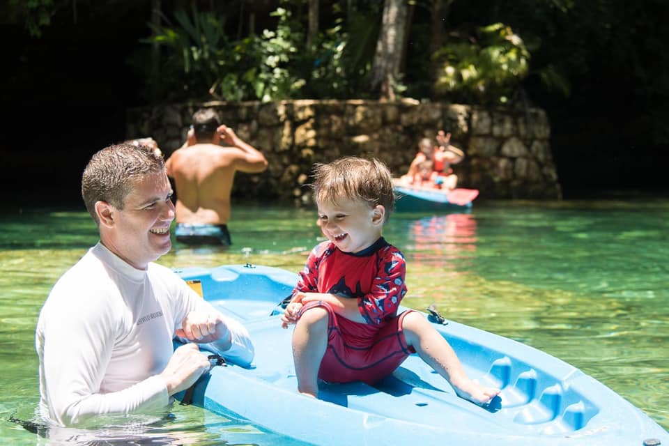 A dad holds onto a paddleboard holding his young son in a cenote in Playa del Carmen, one of the best things to do in Playa del Carmen with kids.