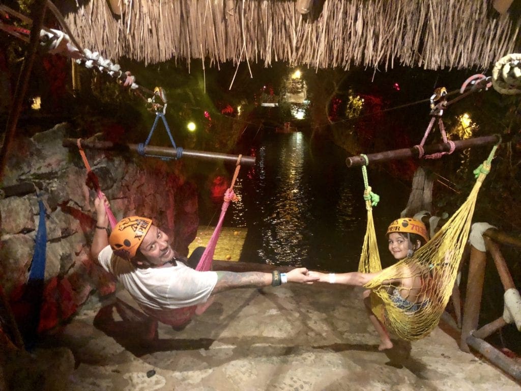 A dad and daughter hold hands as their hammock ziplines are about to take off at Xplor Park, one of the best things to do in Playa del Carmen with kids