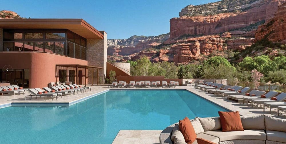 A view of a crystal blue pool a the Enchantment Resort, with hotel buildings and the iconic red rocks in the background.
