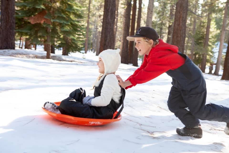 A young boy pushes his little sister on a red sled within Tahoe Donner, one of the best ski resorts near Lake Tahoe for families.
