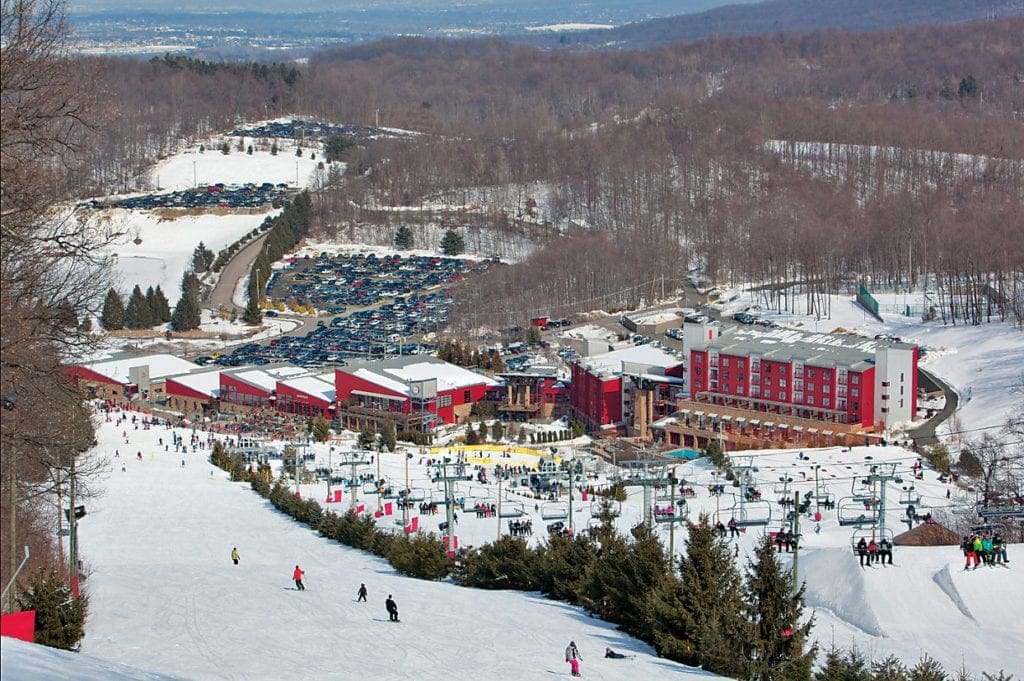 An ariel view of Bear Creek Resort, featuring sevel skiers on the slopes, as well as the on-mountain buildings.