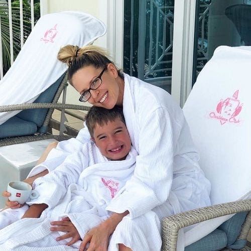 A mom and son sit together on a pool chair, wearing matching robes from Caribbean Club Hotel Grand Cayman.