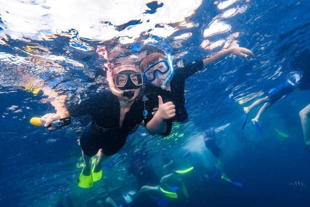 A mom and her young boy snorkel in full wetsuites while exploring the Great Barrier Reef. Protecting exposed skin is one of our tips for snorkeling with kids.