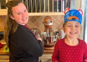 A mom and young girl turn around to smile while baking in the kitchen.