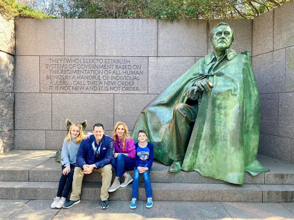 A family of four sits together near a statue in Washington DC, one of the best places to visit during Memorial Day Weekend near NYC for families.
