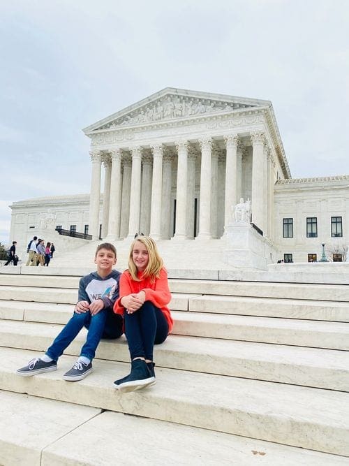 Two kids sit in front of a monument in Washington DC.