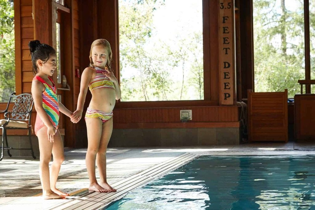 Two girls hold hands while standing at the side of the indoor pool at Mohonk Mountain House.