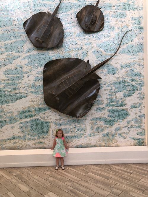 A young girl stands under three sting ray art features on the wall at Grand Cayman Marriott Beach Resort in Grand Cayman.