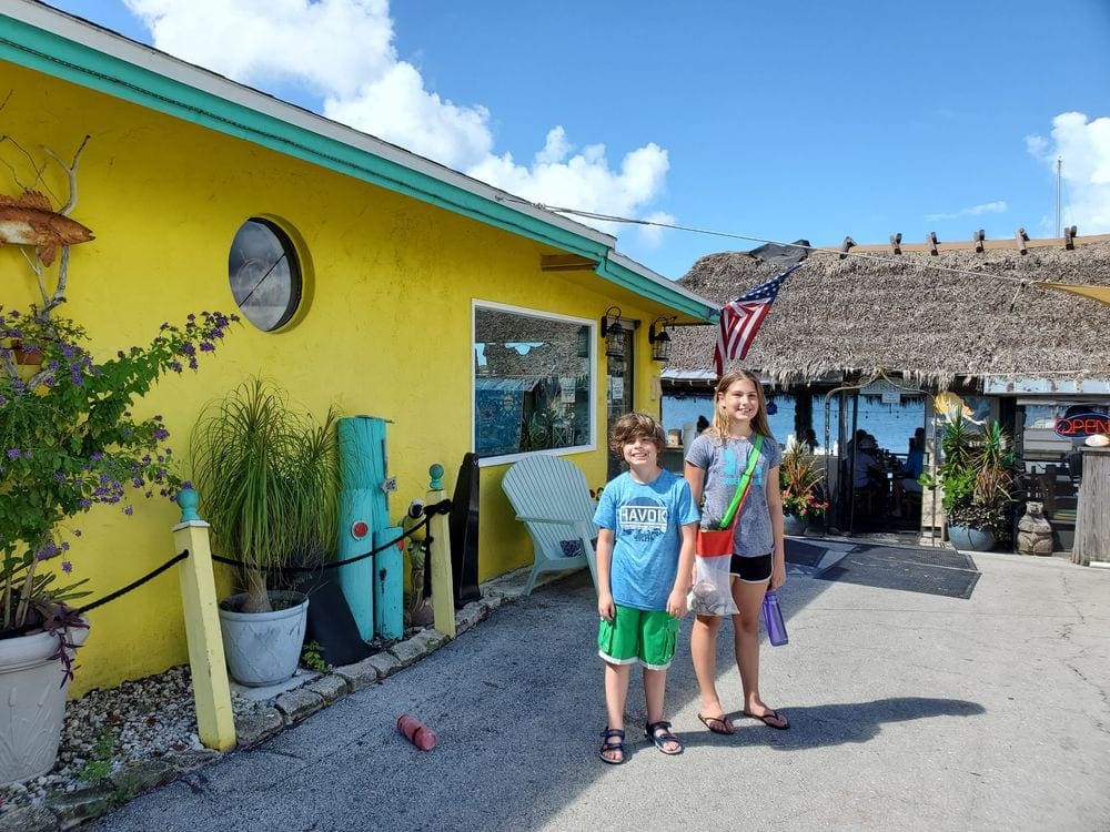 Two kids stand in front of a bright yellow building in Naples, Florida.