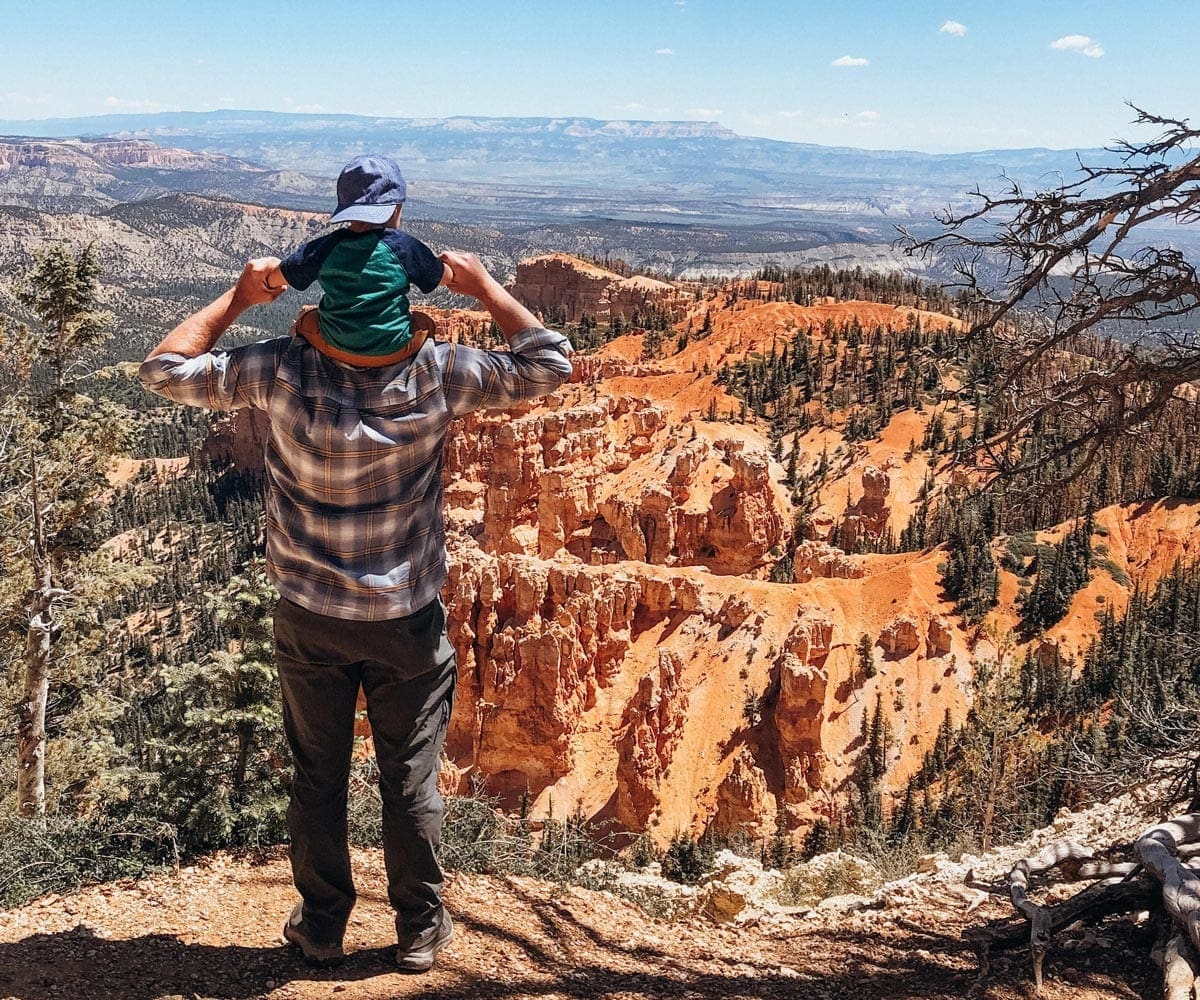 A dad holds his young son on his shoulders looking out onto Bryce National Park.
