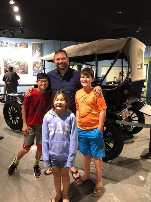 A family of four stands in front of an early Ford card at the Edison Estates in Florida.