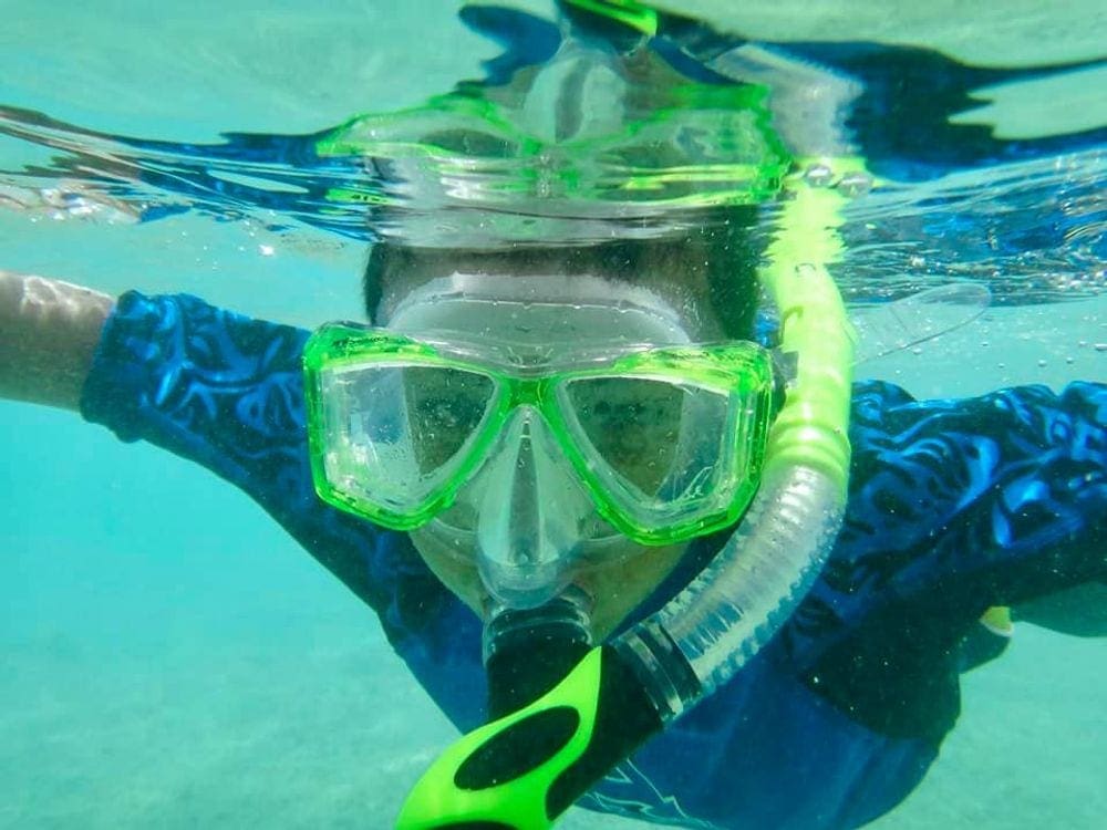 A close up of a young boy wearing lime green snorkel gear while snorkeling in Hanauma Bay, Hawaii.