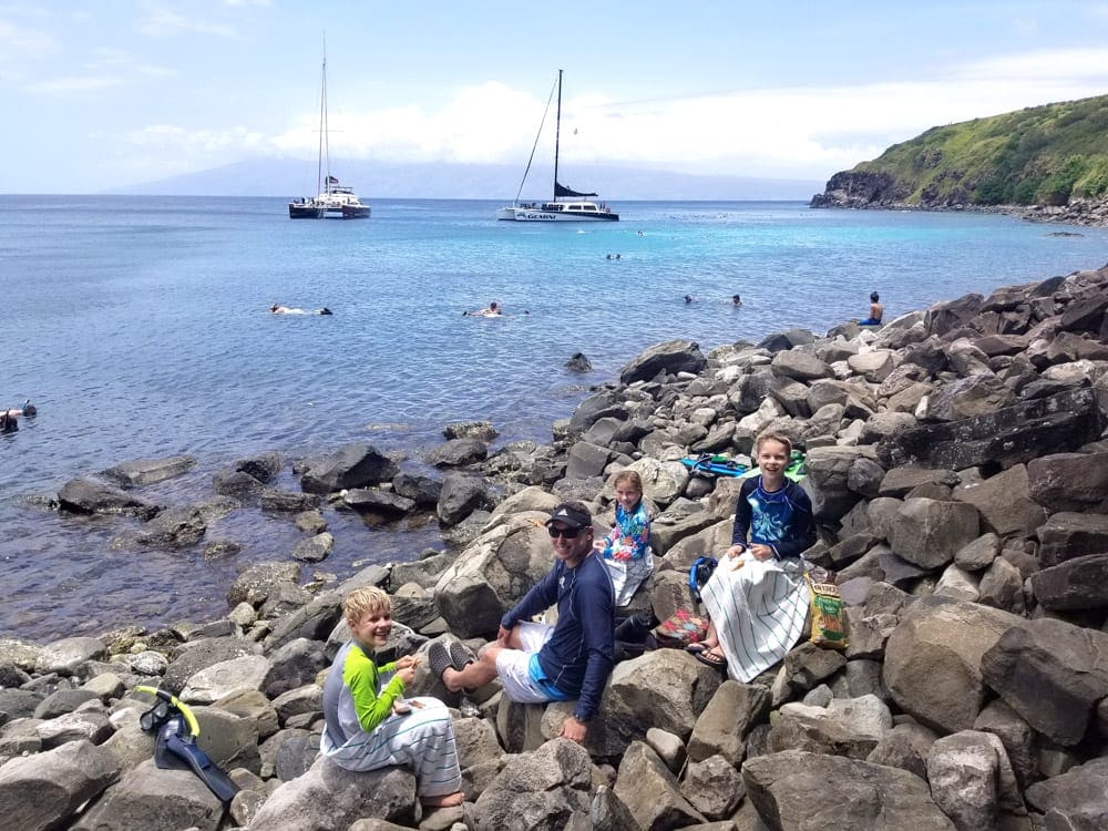 Dad and three kids sit among the rocks in Honolua Bay in Maui.