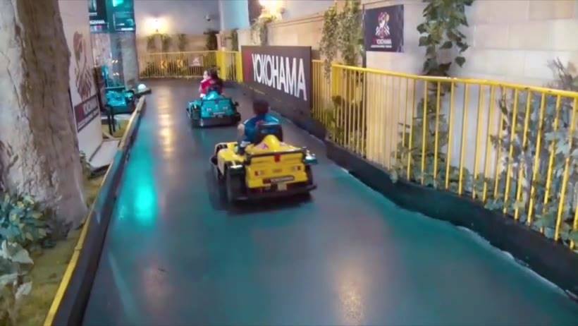 Two kids race around a track in mini cars at Kidzania.