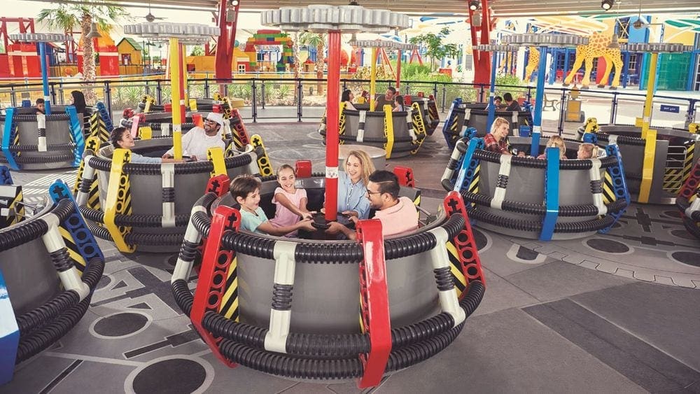 Several cars in an amusement ride at LEGOLAND Dubai carry happy, smiling families.