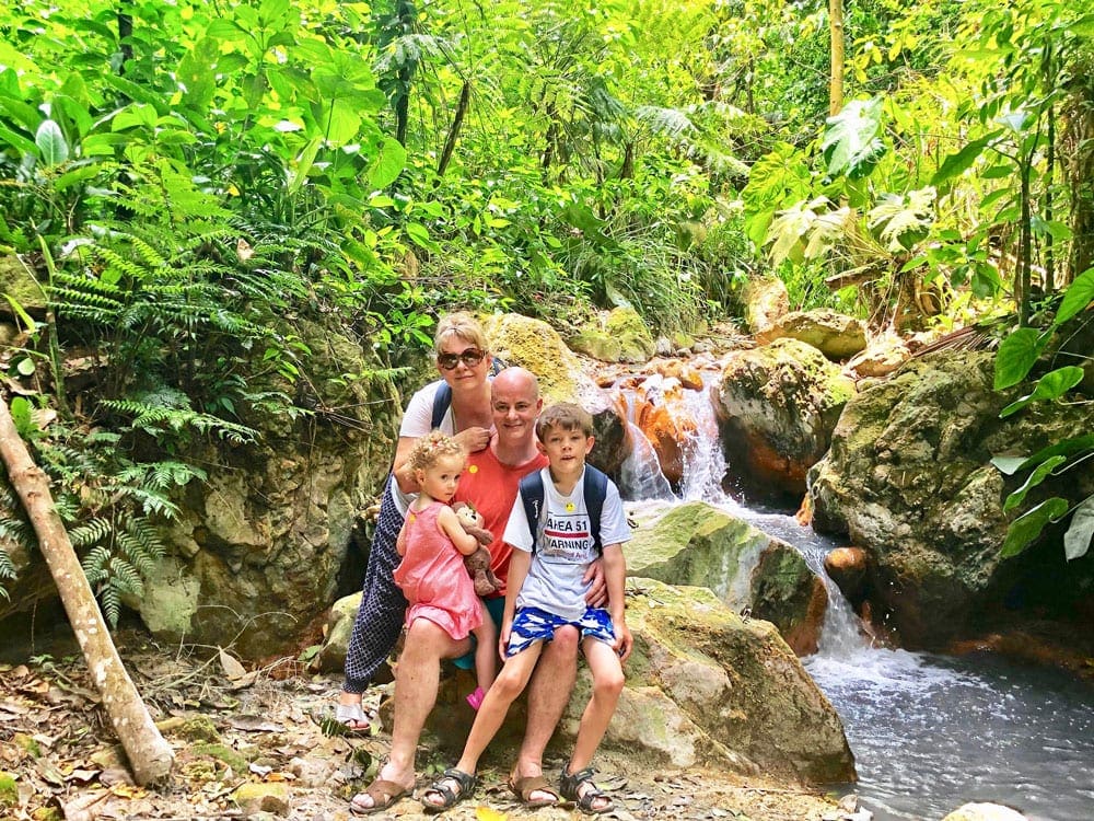 A beautiful famliy poses on rocks among lush foliage.