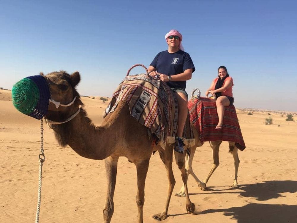 A man and woman ride their own camels on a desert tour in Dubai, one of the best hot places to visit in December for families.