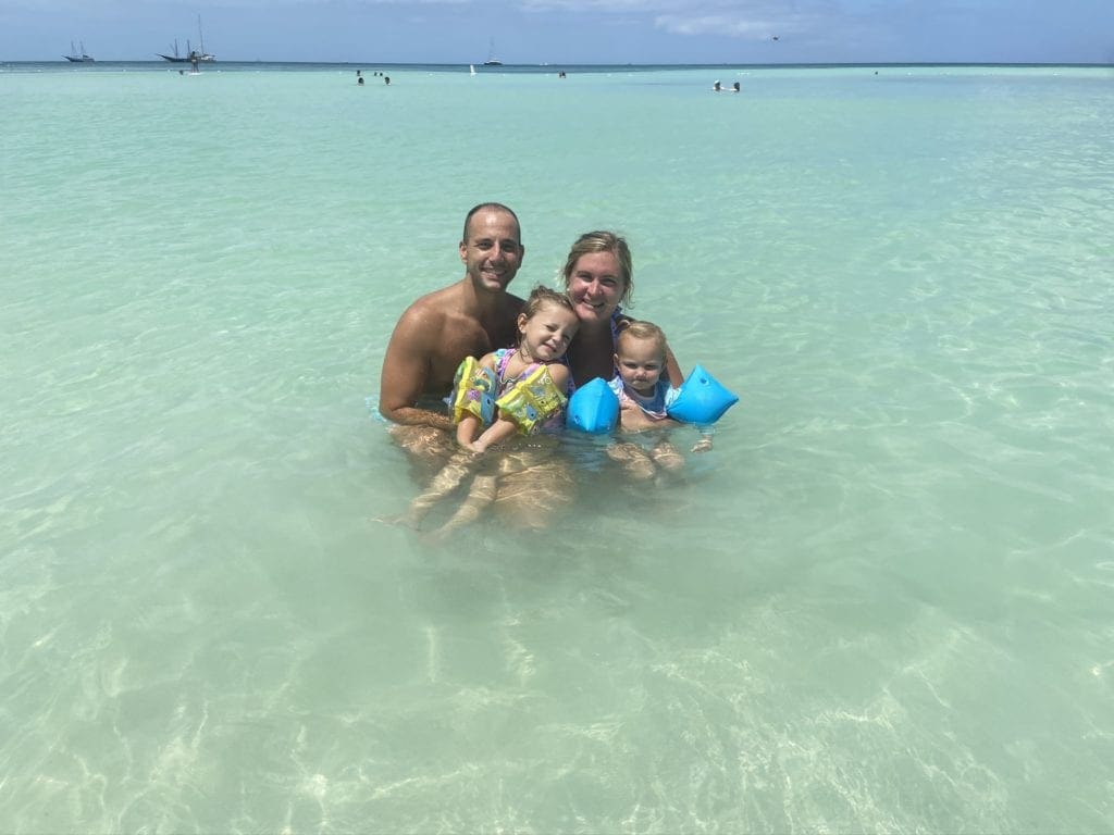 A family of four poses together in the ocean off-shore from the Ritz Carlton in Aruba. Both small girls are wearing arm floaties.