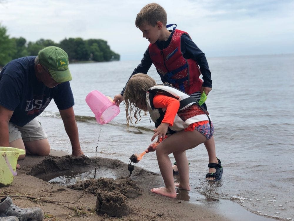 A grandpa and two kids play in the sand at Lake Mill Lacs.