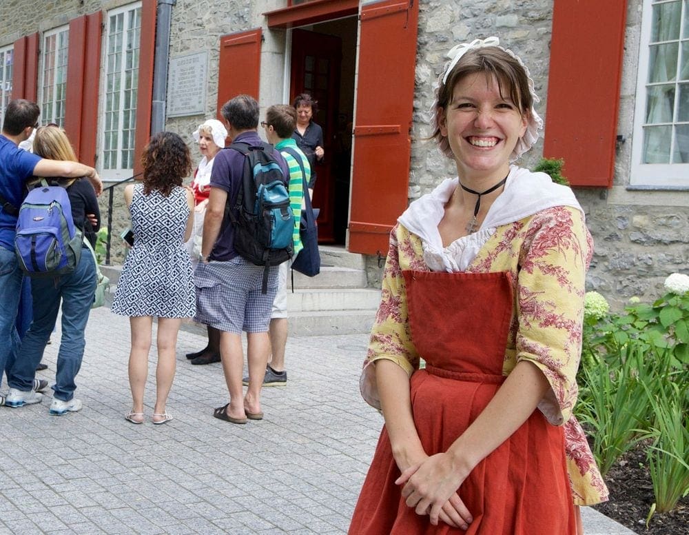 A costumed tour guide at Musée du Château Ramezay smiles while a crowd heads inside one of the on-site buildings.