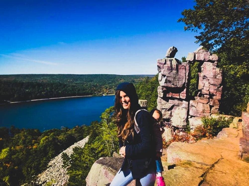 A mom carries her infant on her back with Devils Lake, one of the best lakes in the Midwest for families, in the background.