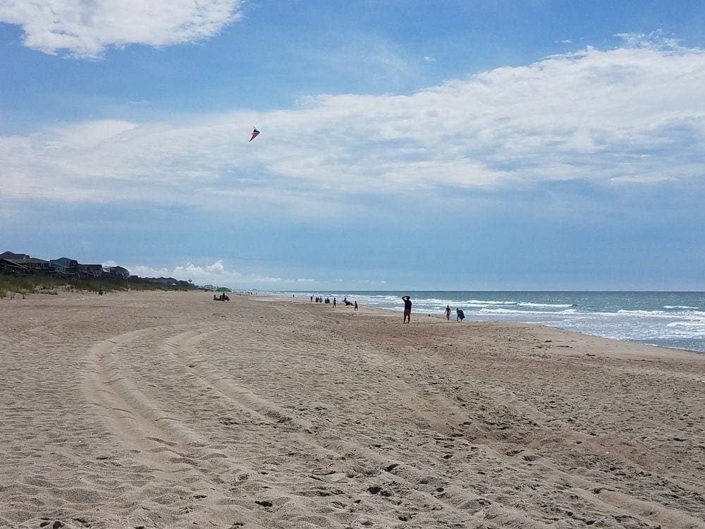 On Emerald Isle, a man flies a kite in the distance on a clear day.