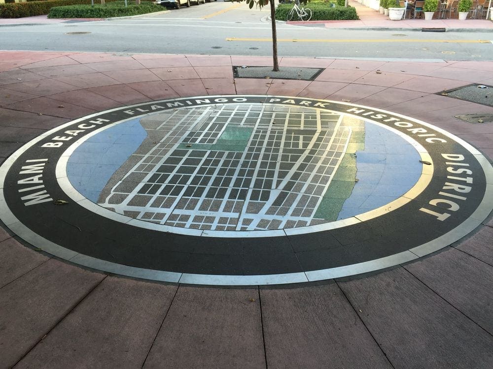 A large emblem on the sidewalk reading "Miami Beach Flamingo Park Historic District".