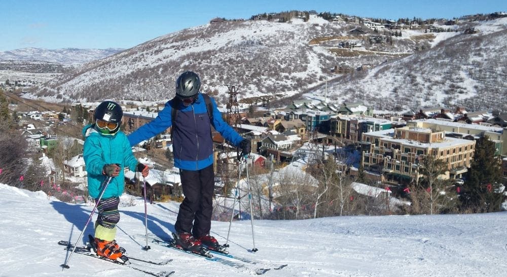 A father and son ski with the mountains behind them in Park City, Utah, one of the top father-son weekend ideas.