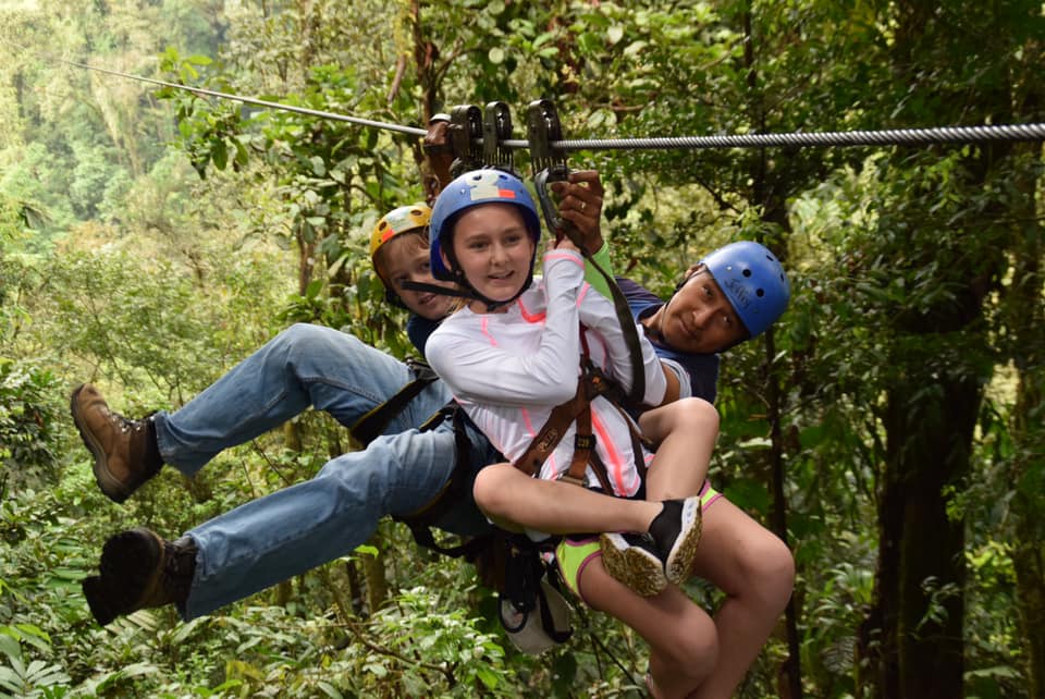 Three people zip-line along a line in the lush green of Costa Rica.