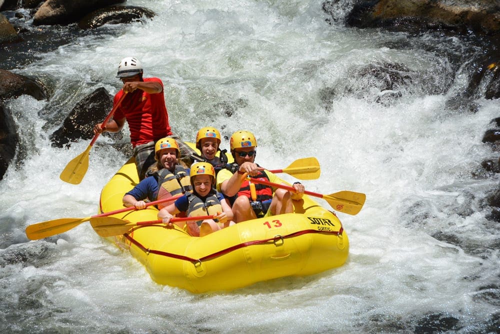 A yellow raft going down a Costa Rican river, carrying four passengers and a guide while on an Adventures by Disney tour.