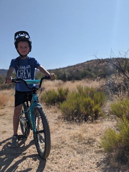 A young boy wearing a helmet stradles a bike while pausing on a trail in Brown's Ranch.