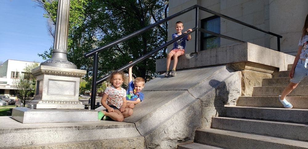 Three kids climb and pose on large steps outside of the City Hall Town Square in Prescotta, Arizona.